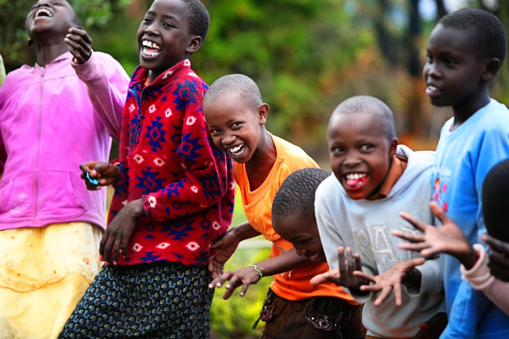 Skrattande kenyanska barn i färgglada kläder som