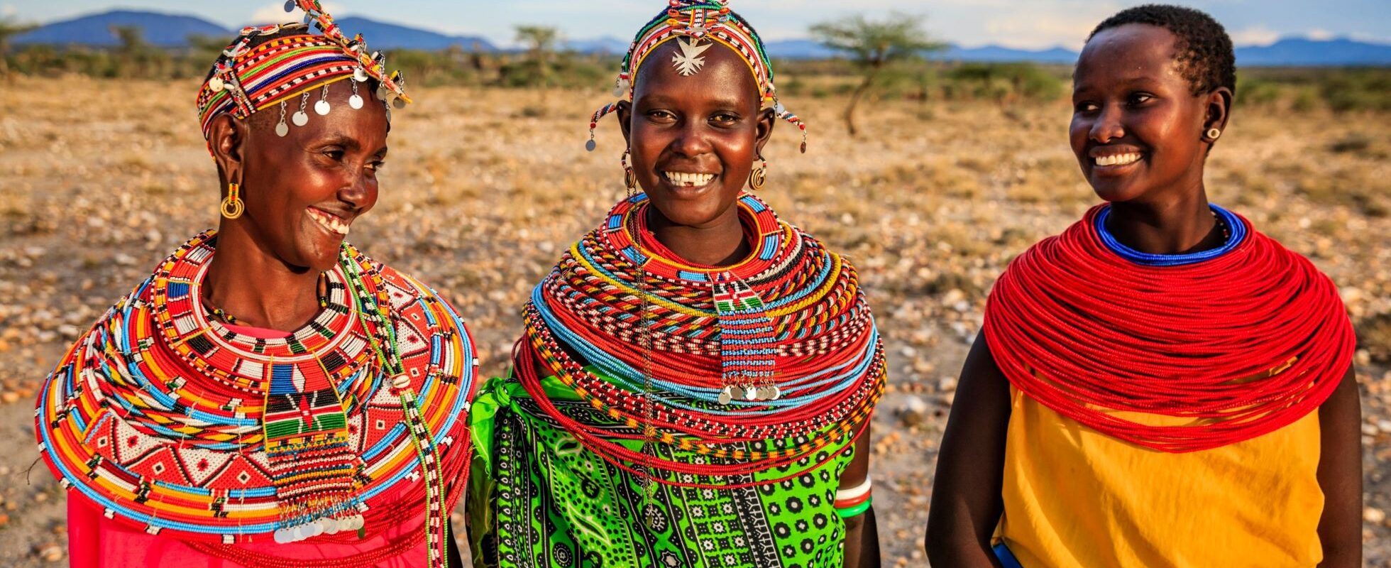 3 kvinnor i Kenya klädda i traditionella färgglada dräkter