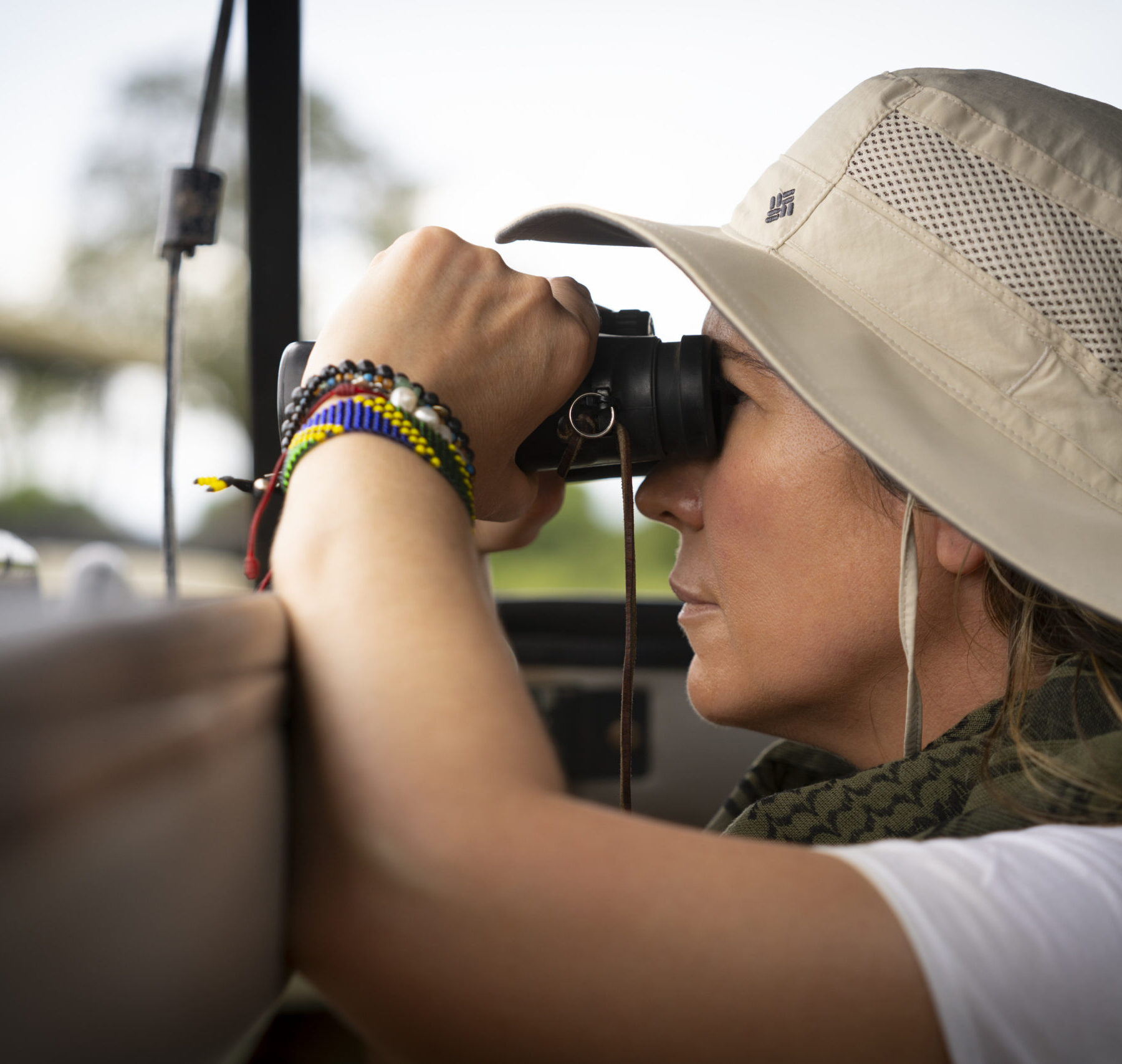 En kvinna med hatt och kikare blickar ut från ett safarifordon i Serengeti