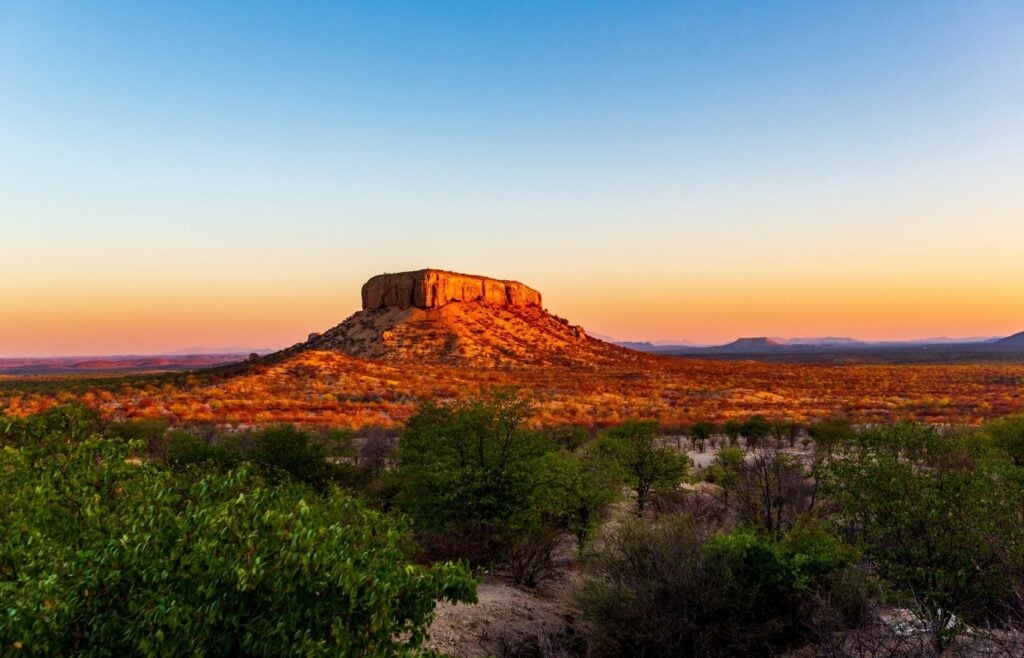 Waterberg-platån i Namibia med ett solbelyst berg och träd på marken framför